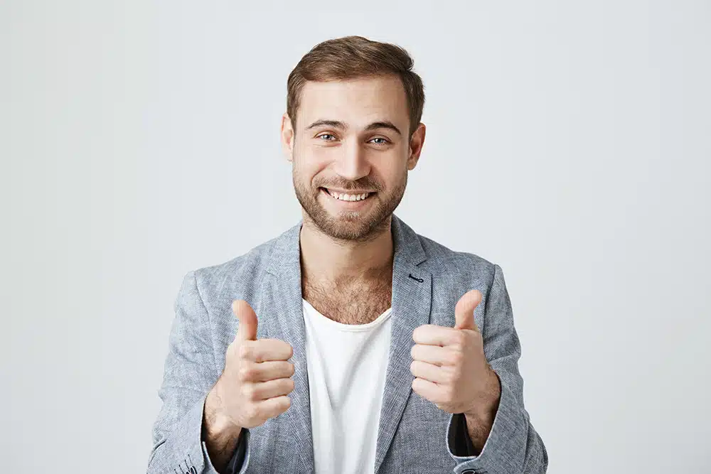 Smiling man giving a double thumbs-up gesture, exuding confidence and positivity.